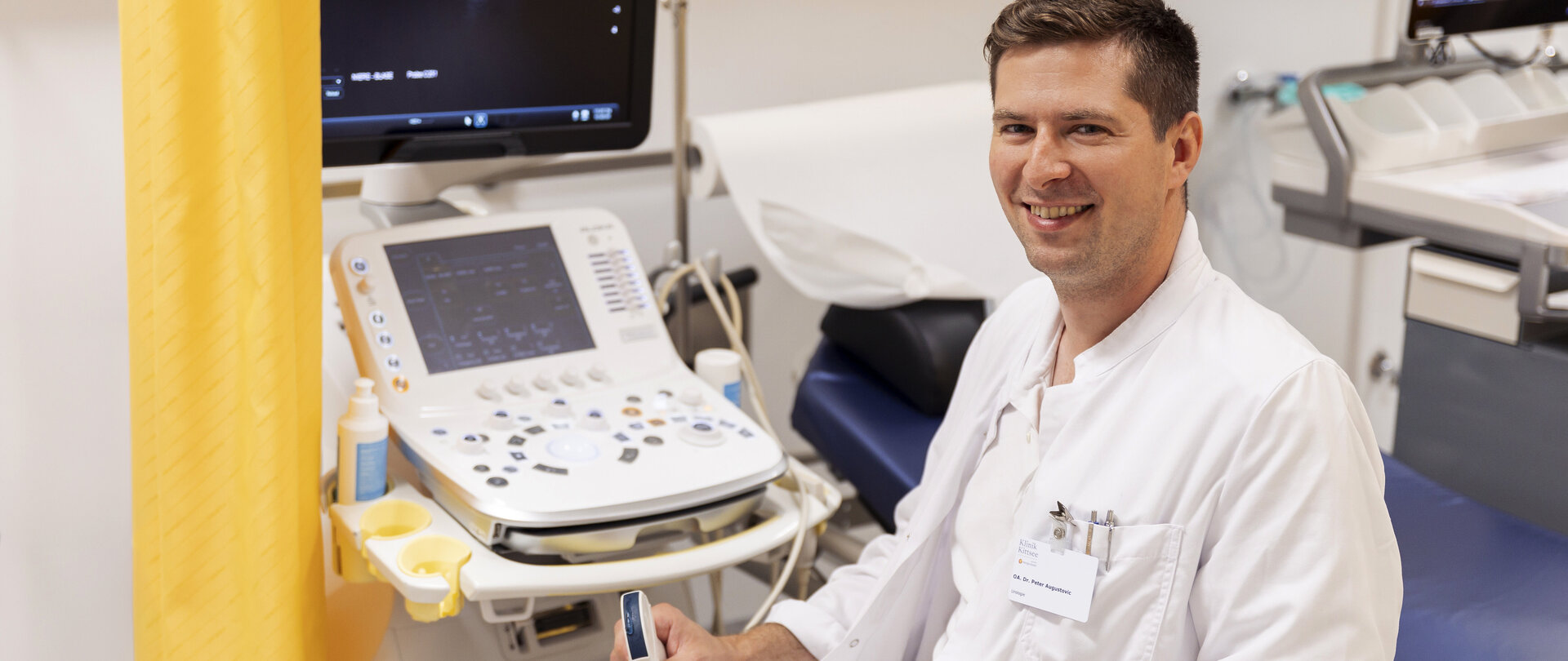 Foto: Sascha Wurzinger Fotografie Junger Arzt im weißen Kittel sitzend neben Ultraschallgerät