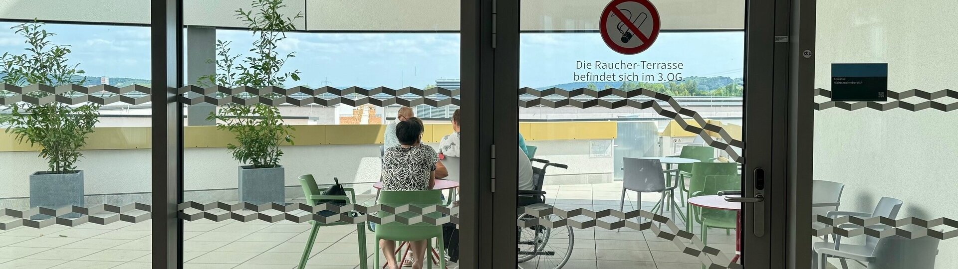 Foto: Gesundheit Burgenland Blick auf eine Terrasse, auf der Tische und Sessel stehen und drei Menschen sitzen
