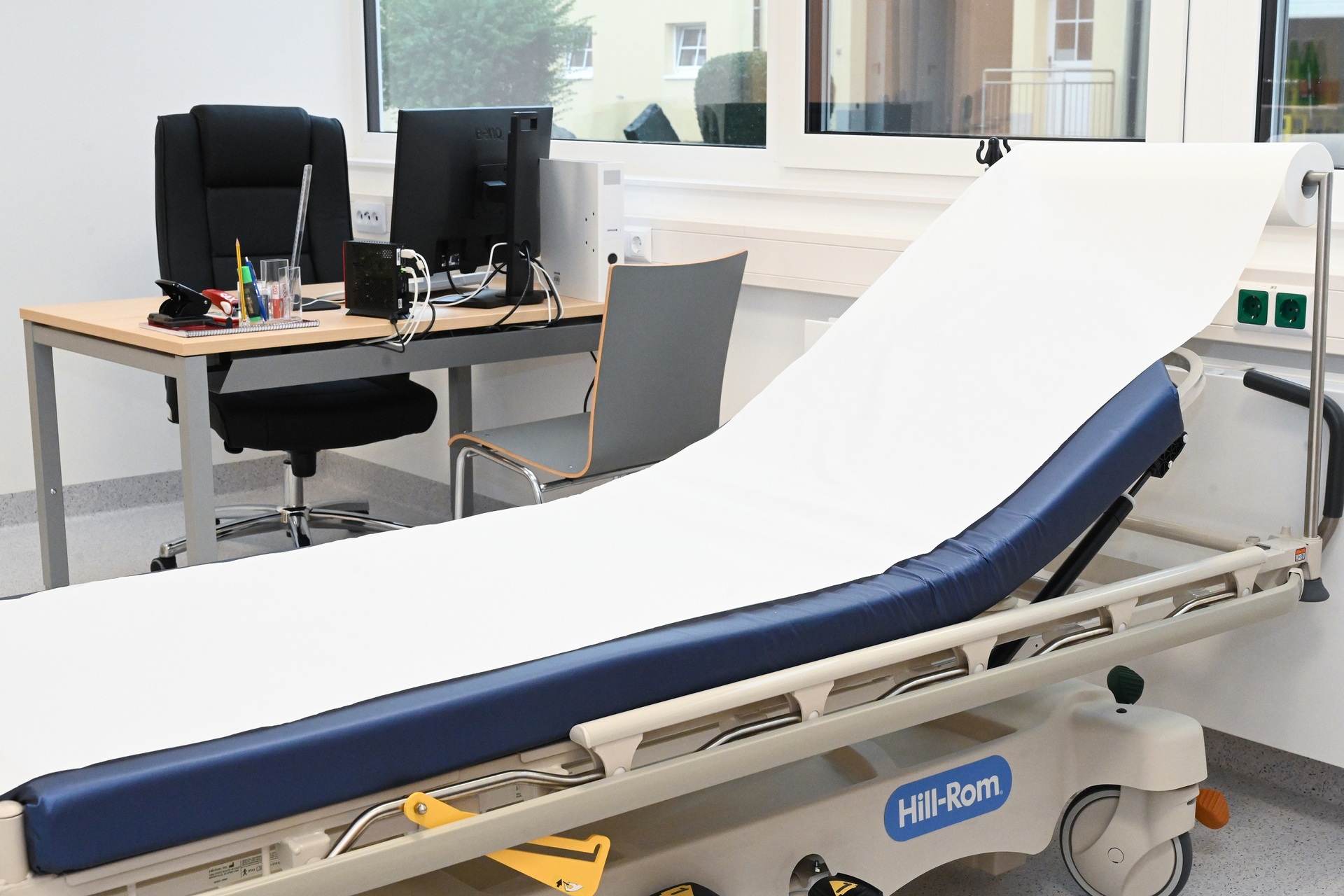Behandlungsbett mit Schreibtisch und PC dahinter