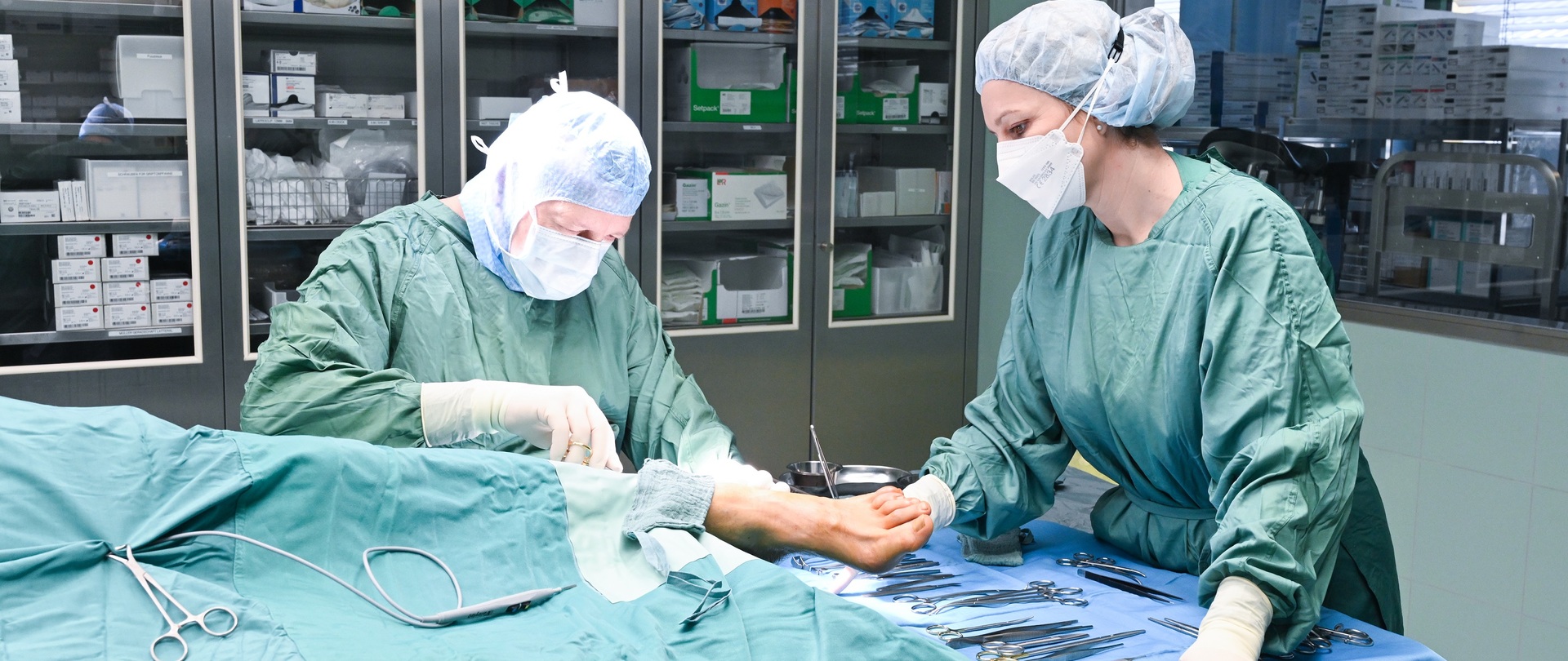 Ein Mann und eine Frau in OP-Kleidung stehen an einem OP-Tisch, zu sehen ist ein Fuß