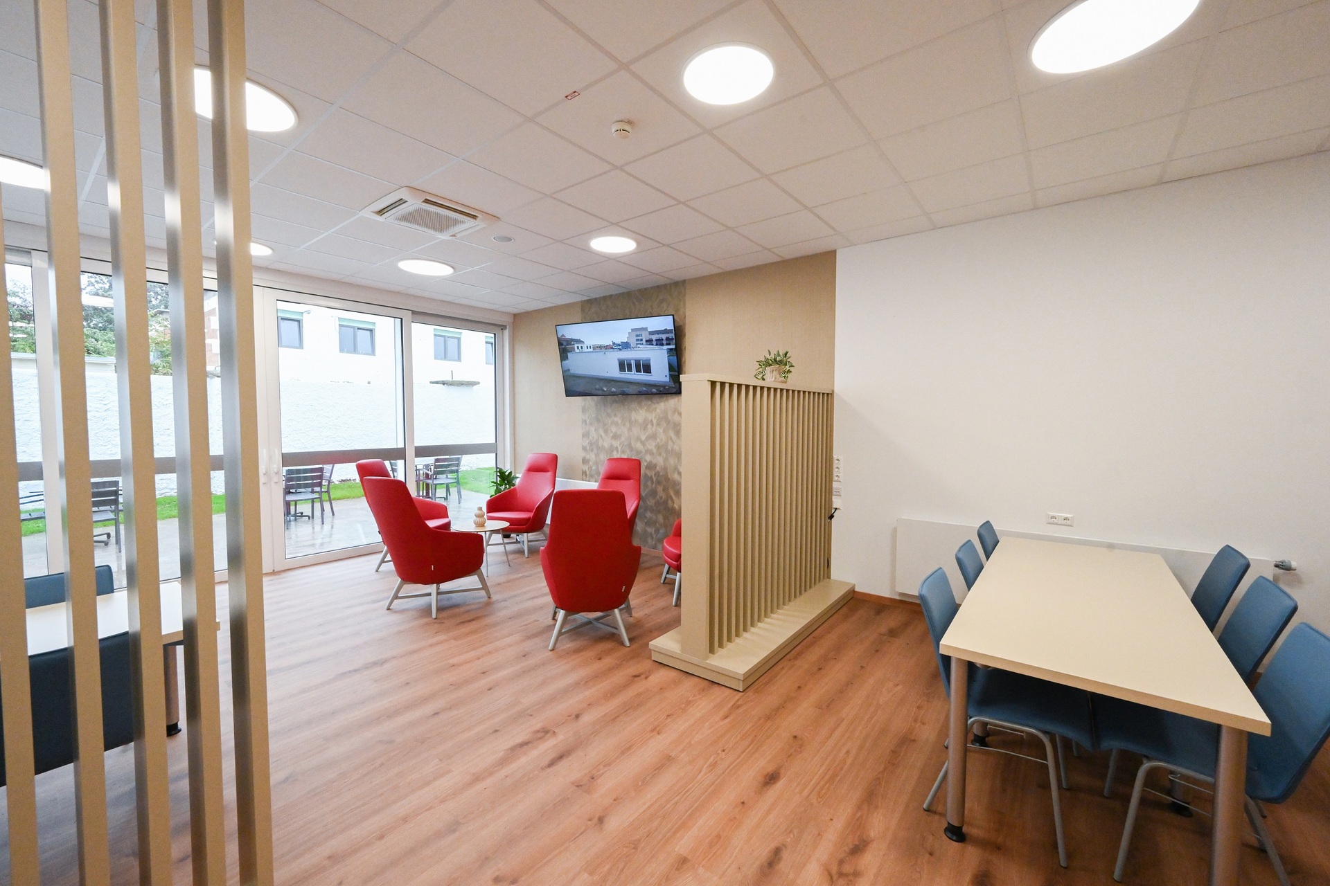 Aufenthaltsraum, rechts ein Tisch mit Stühlen, links mehrere bequeme rote Stühle