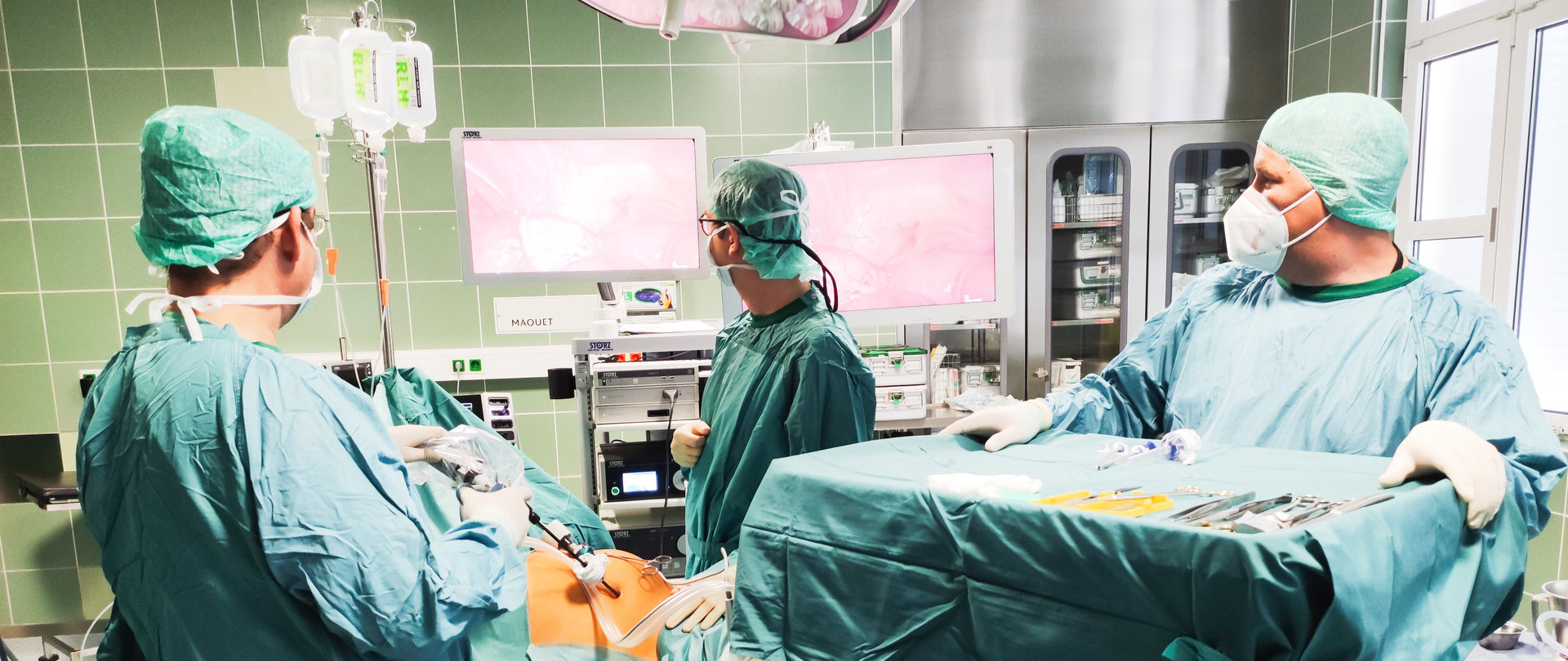 Drei Personen mit Masken im OP-Outfit in einem OP-Saal