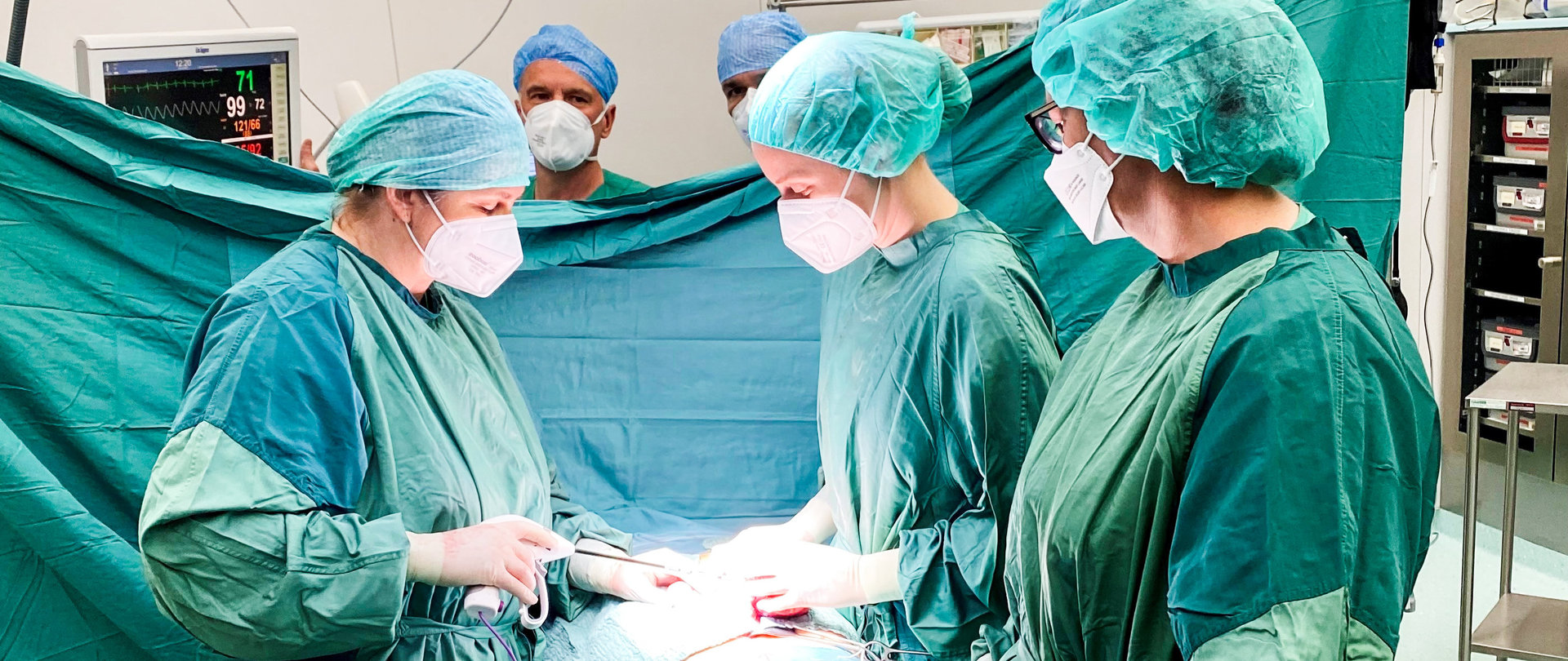 Ein Team aus medizinischem Personal beim Eingriff im OP-Saal. alle sind in Grün gekleidet und tragen Mundschutz
