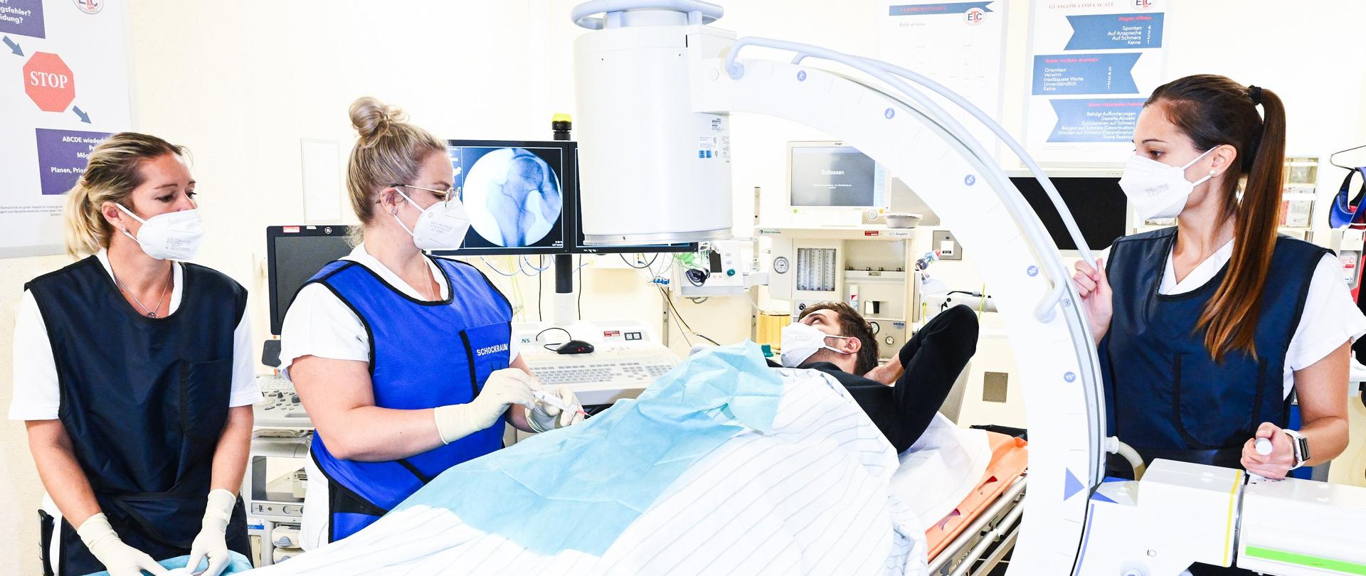 Behandlung von jungem Patienten an Hüfte von Ärztin und zwei Pflegefachkräften